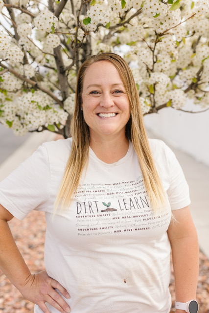 Shalece, play-based facilitator at Dirt Learning, smiling in a Dirt Learning t-shirt beneath a blossoming tree