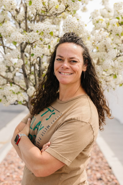 Christi Warr, founder and play-based facilitator at Dirt Learning, with arms crossed beneath a blossoming tree