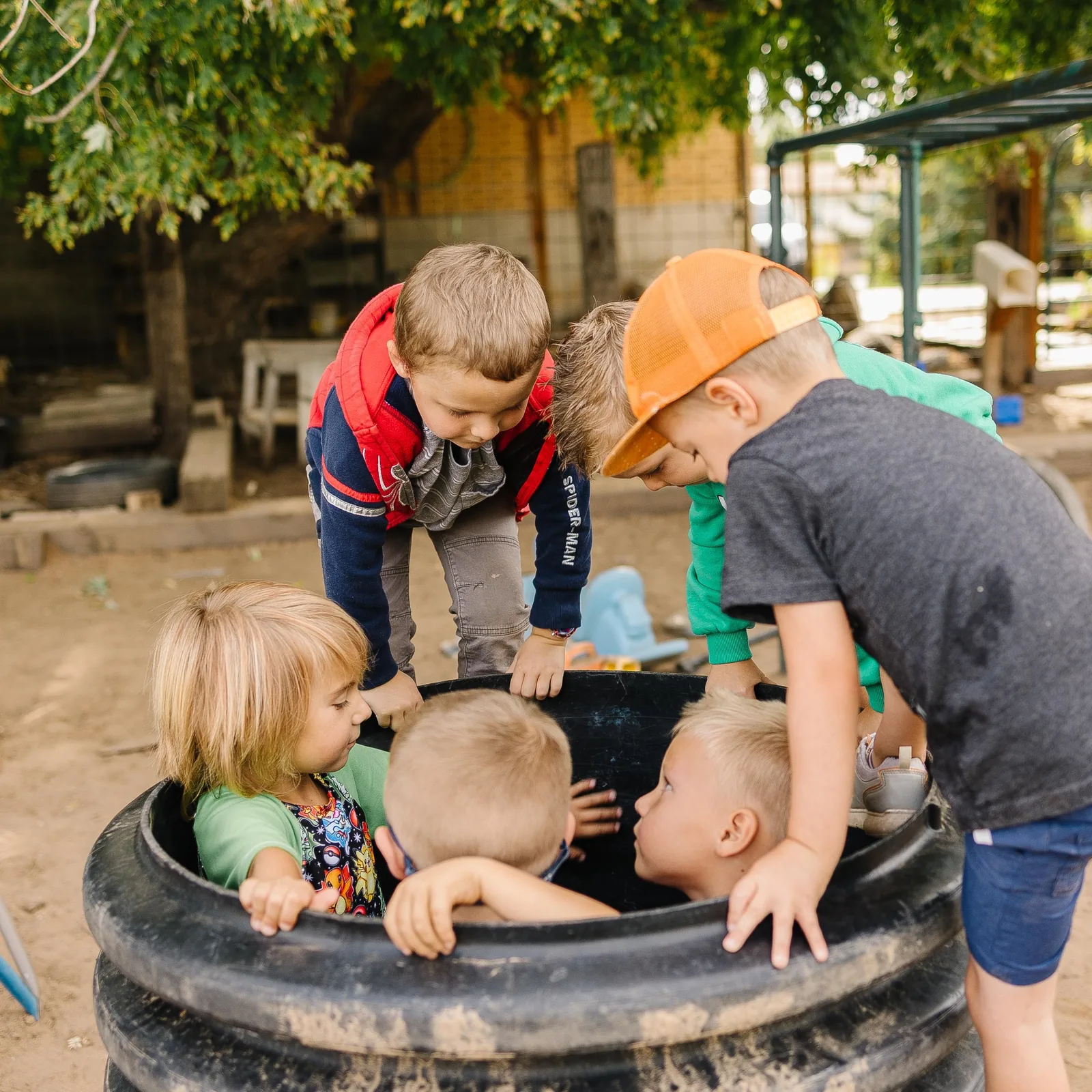 Five children gathered in and around a big black tire, leaning in together to look at something inside