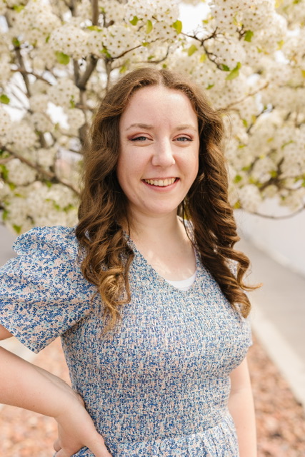 Maecie, play-based facilitator at Dirt Learning, smiling beneath a blossoming tree